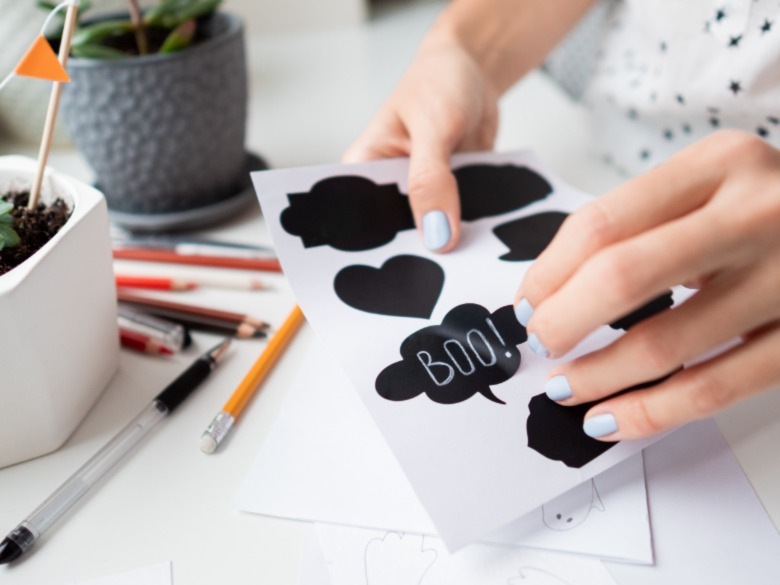 Woman writes Boo! on decorative black stickers for flower pots. Handmade decorations for Halloween.